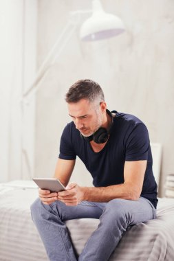 Beyaz adam yatakta yatak odasında oturma ve tablet kullanarak kırklı.