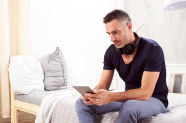 Beyaz adam yatakta yatak odasında oturma ve tablet kullanarak kırklı.