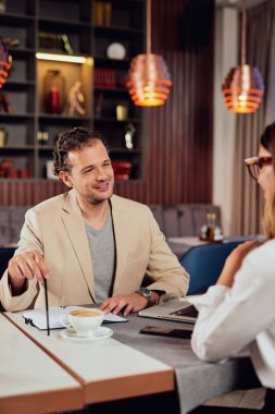 İki çok kültürlü gülümseyen meslektaşları restoranda oturan akıllı rahat giyinmiş ve proje hakkında tartışıyor.