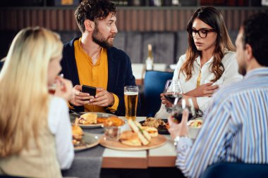 Çok ırklı arkadaşlar restoranda oturan, alkol içme, sohbet ve akşam yemeği için hamburger yeme.