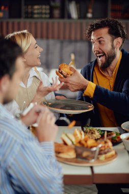 Çok ırklı arkadaşlar restoranda oturan, alkol içme, sohbet ve akşam yemeği için hamburger yeme.
