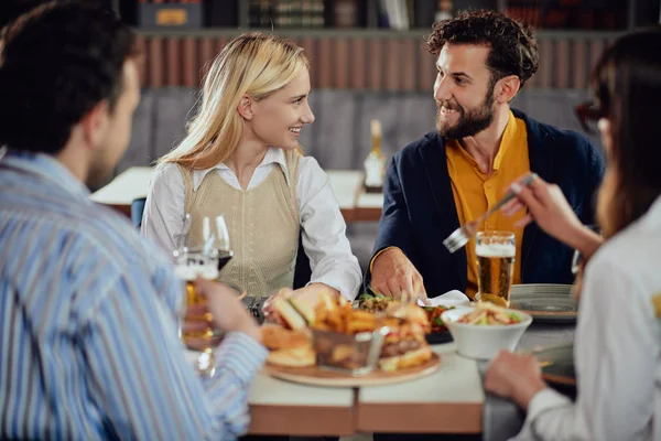 Multi-etnische vrienden zittend in Restaurant, het drinken van alcohol, chatten en het hebben van hamburgers voor het diner. — Stockfoto