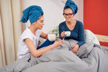 Yatak odasında yatakta oturan, kahve içen ve dedikodu başında havlu ile iki güzel Kafkas kız.