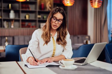 Kafe 'de oturan ve gündemde görevler yazan güzel, ciddi, beyaz bir esmer kız. Uzak iş konsepti.