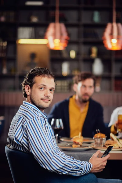 Молодий арабський чоловік одягнений розумний випадковий сидячи за вечерею в ресторані і використовуючи смартфон . — стокове фото