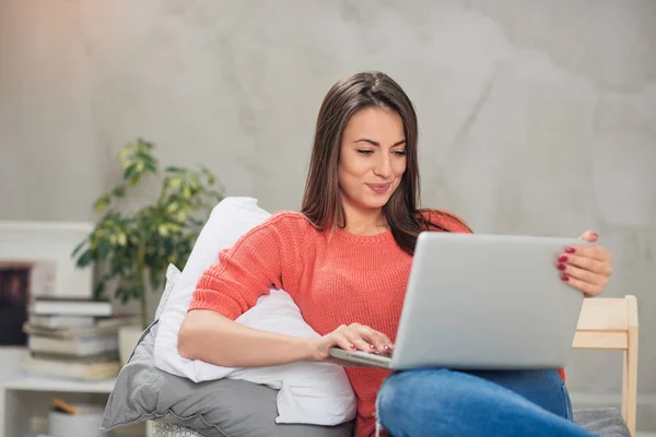 Beautiful Caucasian brunette sitting on the bed in bedroom and using laptop. — Stock Photo, Image
