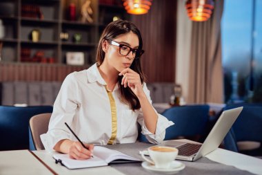 Kafe 'de oturmuş lapotp' a bakıyor ve gündemde görevler yazıyor. Uzak iş konsepti.
