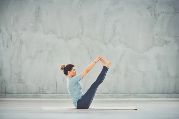 Tekne yoga pozisyonda paspas üzerinde oturan mavi spor giyim güzel Kafkas esmer. — Stok fotoğraf