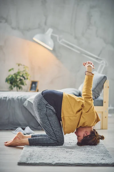 Schöne kaukasische Brünette macht Kopfstand Yoga-Pose im Schlafzimmer auf Teppich. — Stockfoto