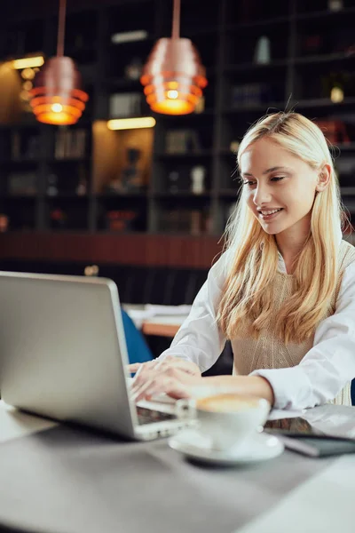 Güzel gülümseyen Kafkas sarışın kadın Blogger giyinmiş akıllı Casual kafeteryada oturma ve dizüstü bilgisayar kullanarak. — Stok fotoğraf