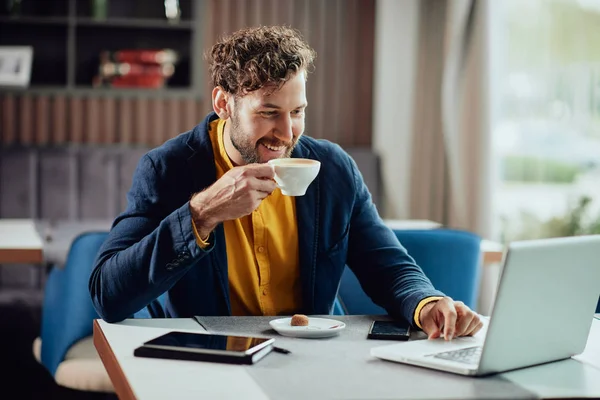 Close-up van bebaarde lachende blanke freelancer zittend in café, het drinken van verse koffie en het gebruik van lapotp. — Stockfoto