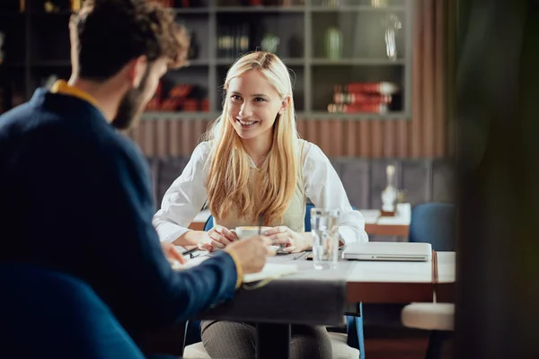 Glimlachend blanke blonde zakenvrouw gekleed Smart Casual discussiëren met haar mannelijke collega over project terwijl zittend in koffieshop. — Stockfoto