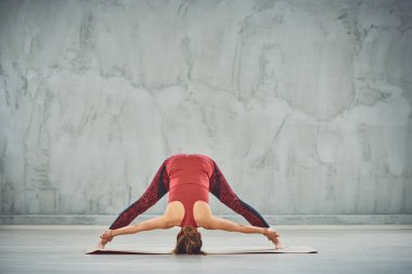 Kırmızı spor giyim Güzel ince esmer Mat yalınayak Geniş Bacaklı İleri Bend Iv yoga poz yapıyor.