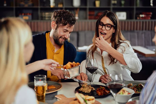 Amici multietnici seduti al ristorante, bevendo alcol, chiacchierando e mangiando hamburger per cena . — Foto Stock