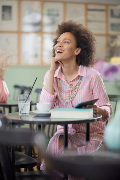 Aantrekkelijke mixed race vrouw in gestreepte roze jurk zitten in Cafe en het gebruik van Tablet. — Stockfoto