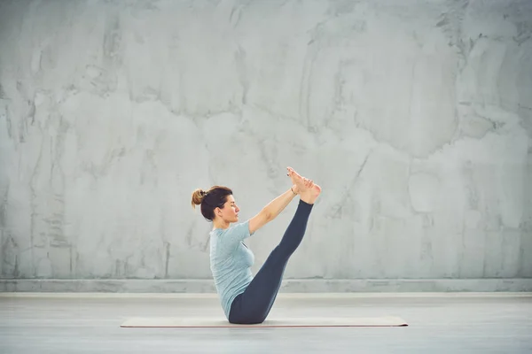 Tekne yoga pozisyonda paspas üzerinde oturan mavi spor giyim güzel Kafkas esmer. — Stok fotoğraf