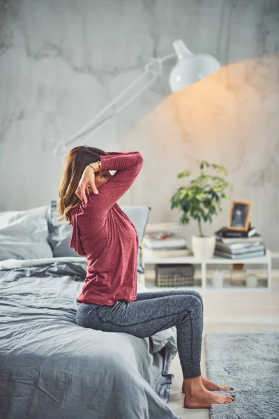 Affascinante bruna caucasica seduta sul letto in camera da letto e facendo esercizi di yoga . — Foto Stock