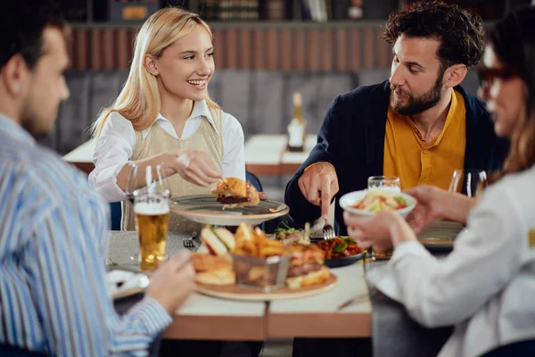 Multietnické přátele, kteří sedí v restauraci, konzumují alkohol, chatují a mají hamburgery na večeři. — Stock fotografie