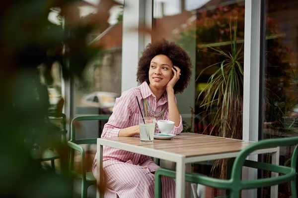 Atrakcyjna kobieta mieszane wyścigu siedzi w kawiarni i korzystających z jej kawy. — Zdjęcie stockowe
