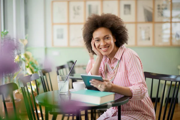 Aantrekkelijke mixed race vrouw in gestreepte roze jurk zitten in Cafe en het gebruik van Tablet. — Stockfoto