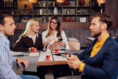 Çok ırklı arkadaşlar kafede oturan giyinmiş, kahve içme, sohbet ve akıllı telefonlar kullanarak.