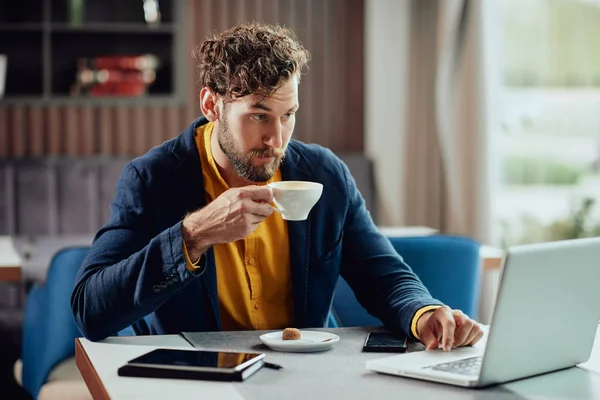 Genç ciddi girişimci akıllı rahat içme espresso giyinmiş ve kahve dükkanında laptop kullanarak. — Stok fotoğraf