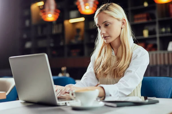 Mladý seriózní kavkazské blondýny businesswoman oblečený inteligentní ležérní sezení v kavárně a pomocí notebooku. — Stock fotografie