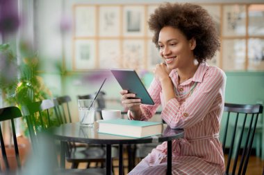 Çekici karışık yarış kadın çizgili pembe elbise kafede oturan ve tablet kullanarak.