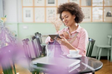 Çekici karışık yarış kadın çizgili pembe elbise kafede oturan ve tablet kullanarak.
