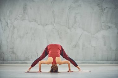 Kırmızı spor giyim güzel ince esmer Geniş Bacaklı İleri Viraj I yoga mat yalınayak poz yapıyor.