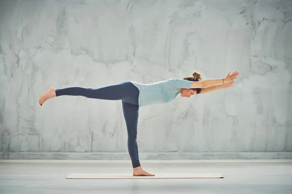 Side view of beautiful Caucasian woman standing on the mat in Warrior III yoga posture. — Stock Photo, Image