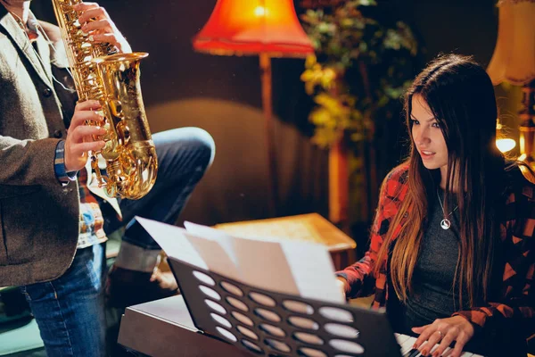 Caucásico hombre jugando saxofón en casa estudio mientras joven talentosa mujer jugando clavier . — Foto de Stock