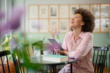 Çekici karışık yarış kadın çizgili pembe elbise kafede oturan ve tablet kullanarak.