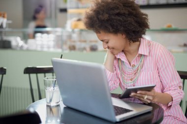 Çekici karışık yarış kadın çizgili pembe elbise kafede oturan ve tablet kullanarak.