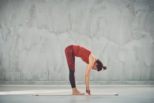 Kırmızı spor güzel Kafkas esmer yan görünümü Standing Forward Bend yoga duruş paspas üzerinde yalınayak ayakta giymek. — Stok fotoğraf