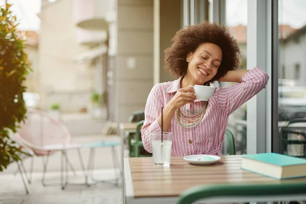 Attraktive Mischlingsfrau sitzt im Café und genießt ihren Kaffee. — Stockfoto