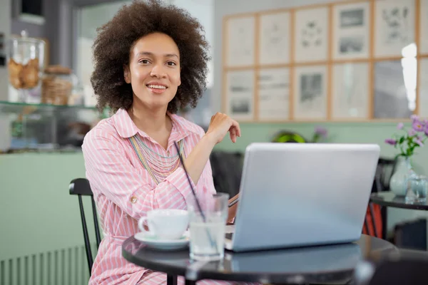 Mooie lachende gemengde race vrouw zittend in café en met behulp van laptop. — Stockfoto