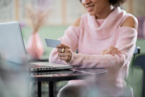 Bella donna mista corsa in maglione collo alto rosa seduto in pasticceria e utilizzando il computer portatile per lo shopping on line . — Foto Stock