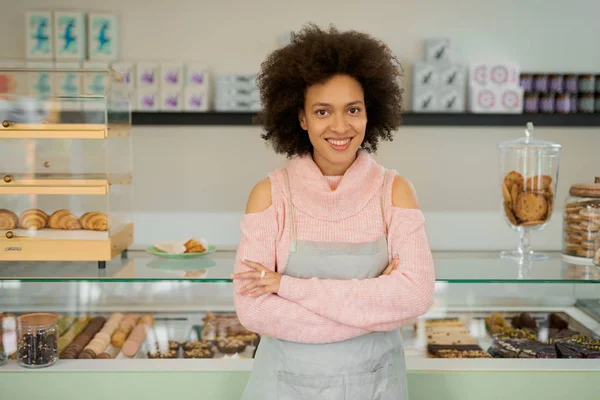 Güzel gülümseyen karışık yarış kadın sahibi pasta dükkanı kollu önlük ayakta giymiş bir dükkan geçti.