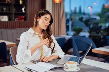 Genç güzel ciddi Kafkas esmer kafede oturan ve gündemde görevleri yazma. Uzak iş kavramı.