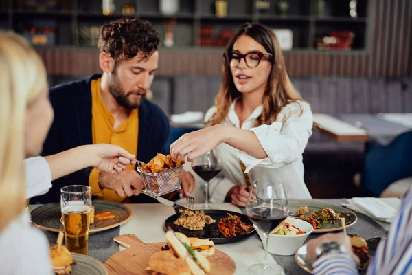 Multietnické přátele, kteří sedí v restauraci, konzumují alkohol, chatují a mají hamburgery na večeři. — Stock fotografie