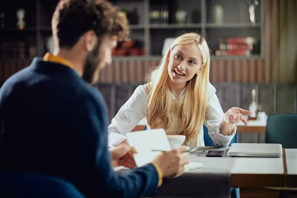 Smiling Caucasian blonde businesswoman dressed smart casual discussing with her male colleague about project while sitting in coffe shop. — Stock Photo, Image