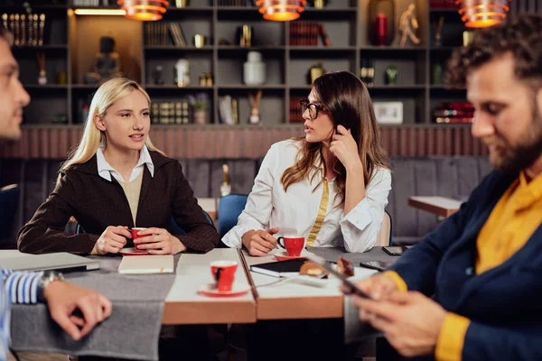 Τέσσερις πολυϊνιες επιτυχημένοι συνάδελφοι που κάθονται στην καφετέρια για διάλλειμα για μεσημεριανό, πίνοντας καφέ και συζητώντας για νέο έργο. — Φωτογραφία Αρχείου