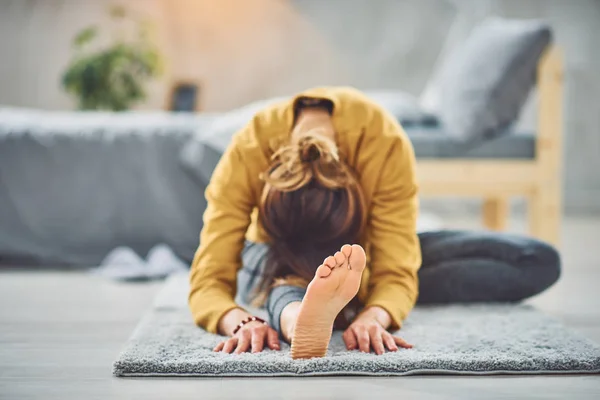 Caucásico morena estiramiento de la pierna mientras está sentado en la alfombra en el dormitorio . — Foto de Stock