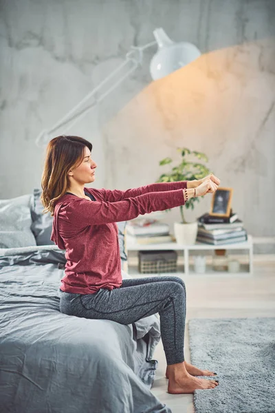 Encantadora morena caucásica sentada en la cama en el dormitorio y haciendo ejercicios de yoga . — Foto de Stock