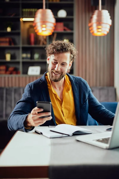 Unga kaukasiska affärsman klädd smart casual med hjälp av smart telefon när du sitter i kaféet. På skrivbordet laptop. — Stockfoto