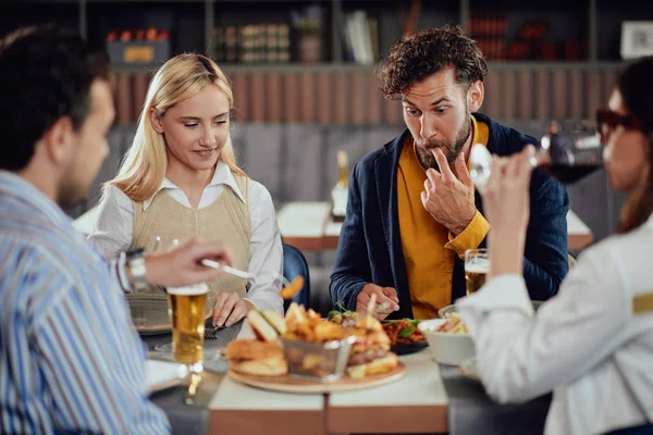 Multiethnic friends sitting at restaurant, drinking alcohol, chatting and having burgers for dinner. — Stock Photo, Image