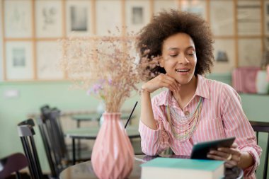 Çekici karışık yarış kadın çizgili pembe elbise kafede oturan ve tablet kullanarak.