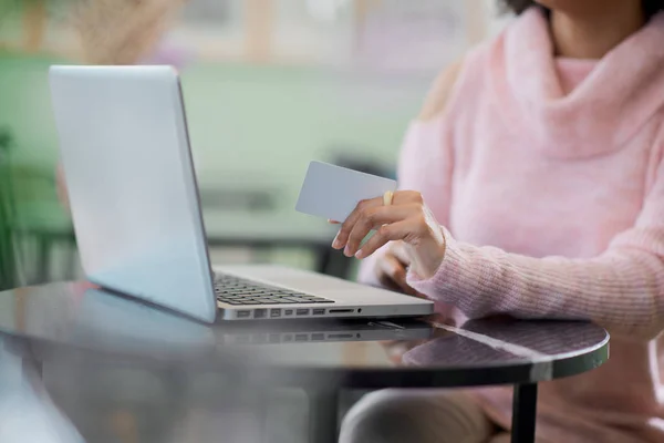 Vacker blandad ras kvinna i rosa polotröja sitter i konditoriet och använder laptop för on line shopping. — Stockfoto