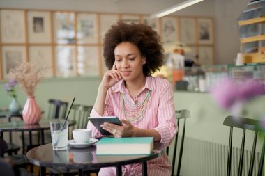 Çekici karışık yarış kadın çizgili pembe elbise kafede oturan ve tablet kullanarak.